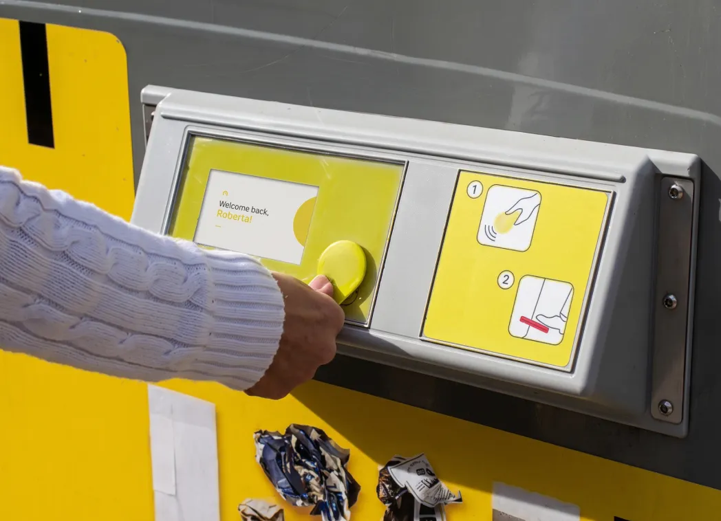 Hand holding an access tag up to the reader of a yellow Genius container